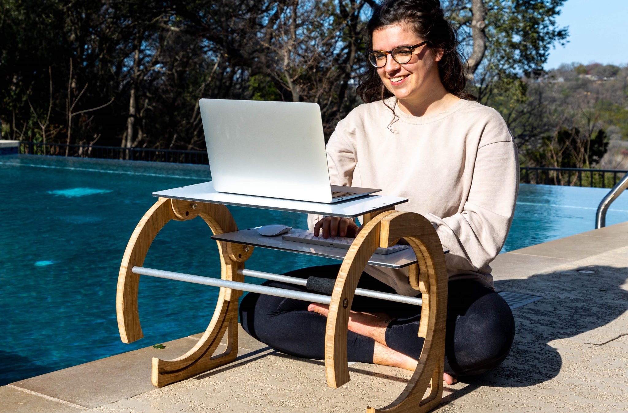 Woman sitting outside by pool cross-legged with laptop desk tray